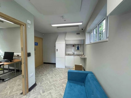 Waiting area in lobby with sofa and small sink area, toilet and door open into room with desk and computer