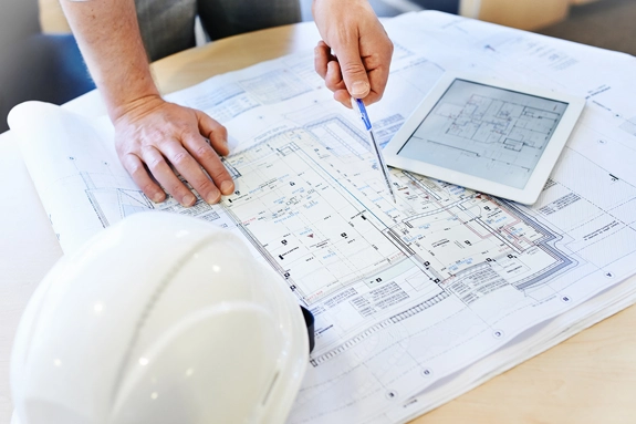 Person looking at Architectural Design building plan on table next to tablet and hard hat